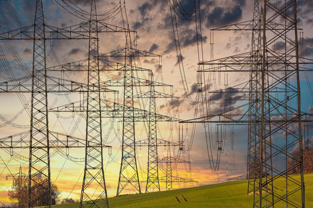 High-voltage electrical transmission towers and power lines at sunset showing the grid infrastructure generators must replicate