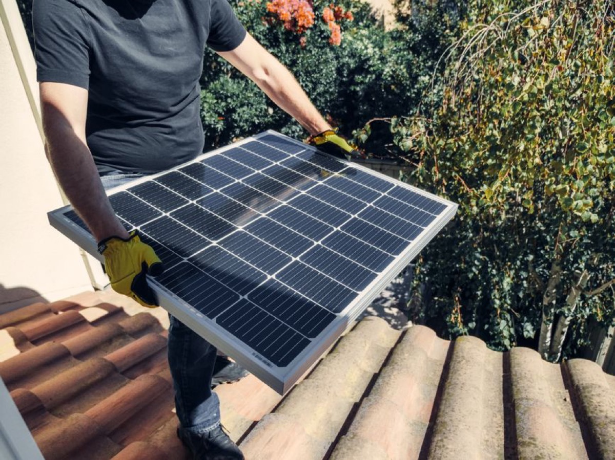 Person installing solar panel on rooftop for home energy system integration